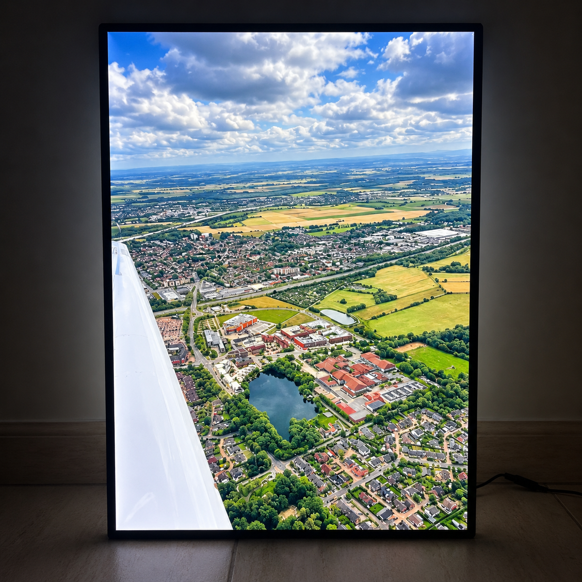 Illuminated wall art showing an aerial view from an airplane over a town, lake and countryside